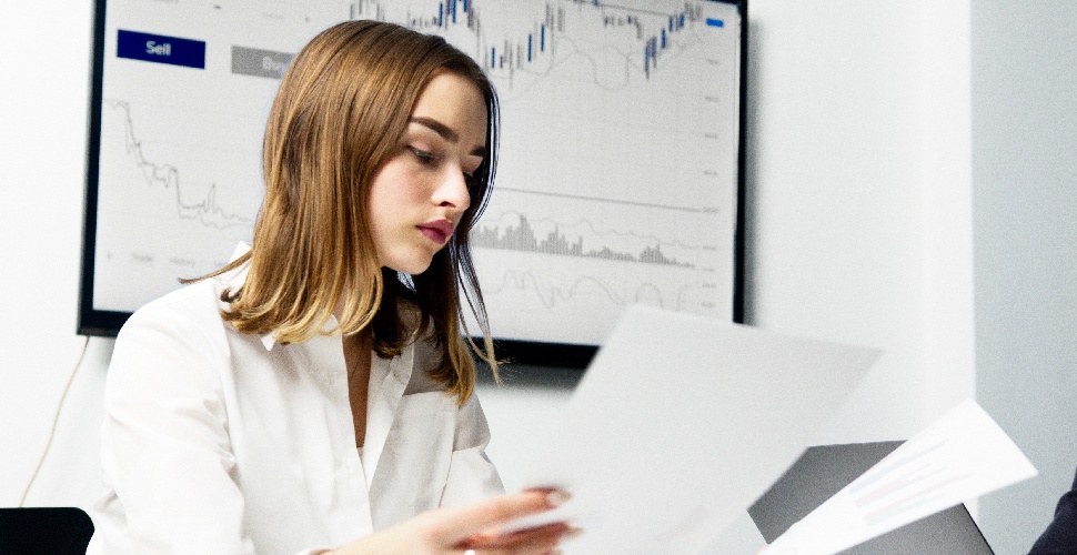 Sitting in front of a chart, a woman in an office setting looks at some paperwork.