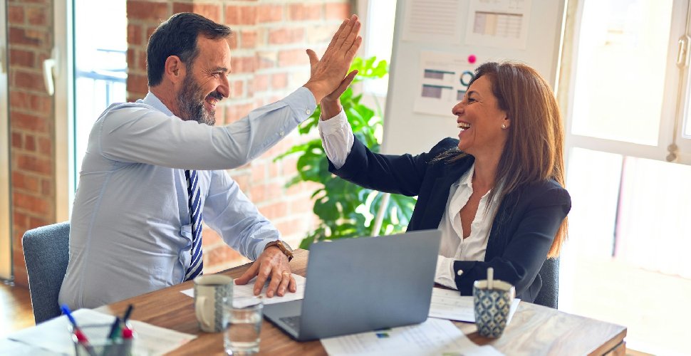 Two middle age business workers smiling happy and confident. Working together with smile on face hand giving high five at the office. Photo by krakenimages on Unsplash