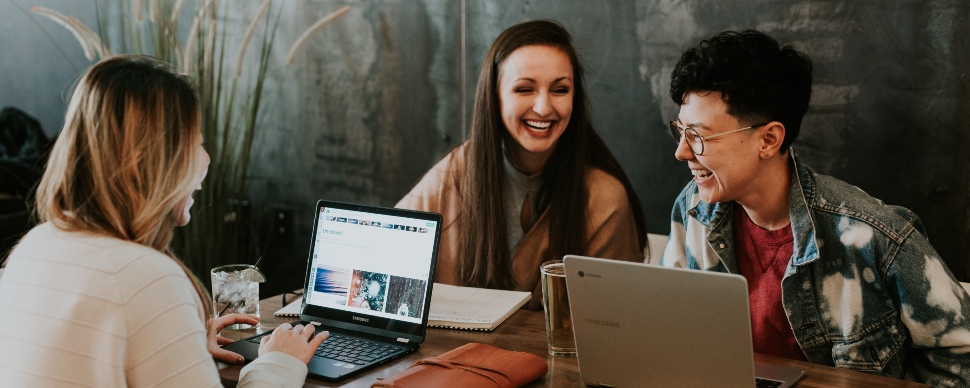 three female contract professionals having a laugh while working on their computers in a cafe setting