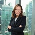 Smiling woman in a business suit standing by a window with city buildings in the background.