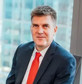 Man in a suit with a red tie sitting by a window.