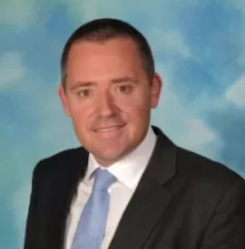 Person in a suit with a blue tie against a cloudy sky background.