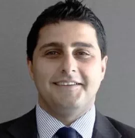 Man in suit smiling against a gray background.
