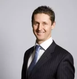 Smiling man in a suit and tie against a gray background.