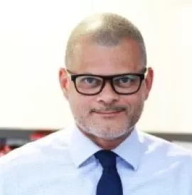 Person with glasses and tie smiling in a bright setting.