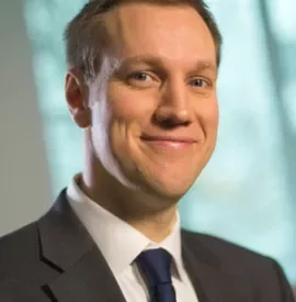 Smiling man in a suit with a blurred window background.