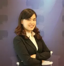 Smiling woman in a black blazer with arms crossed against a purple background.