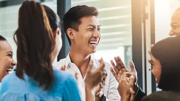 Group of diverse coworkers smiling and clapping in an office setting.