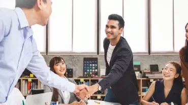 Diverse group of professionals meeting and shaking hands in an office setting.