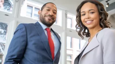 Two professionals smiling inside a modern office space.