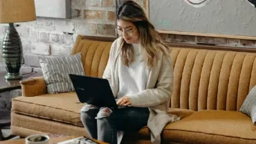 Person sitting on a brown couch using a laptop.