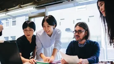A diverse team collaborating around a laptop in a bright office setting.
