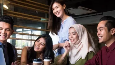 Diverse group of five people smiling around a laptop in an office setting.