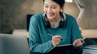 Woman smiling while studying with a laptop at a desk.