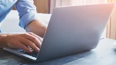 Person typing on a laptop at a wooden desk with a cup of coffee.
