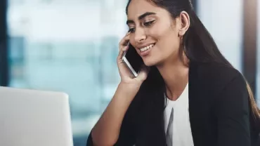Woman talking on a mobile phone while using a laptop in an office setting.