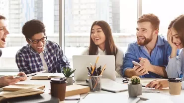 Group of diverse students laughing and studying together in a bright room.