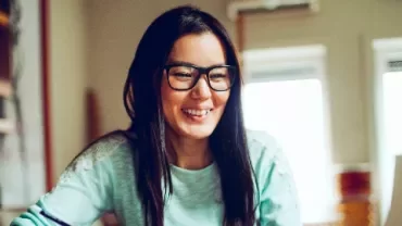 Smiling woman with glasses working on a laptop at home.