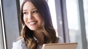 Woman smiling by a window with a tablet