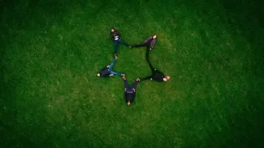 Five people laying on the grass forming a star shape