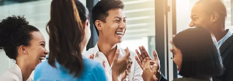 Group of diverse coworkers smiling and clapping in an office setting.