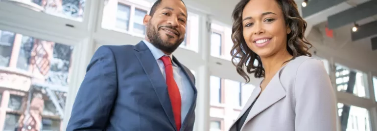 Two professionals smiling inside a modern office space.