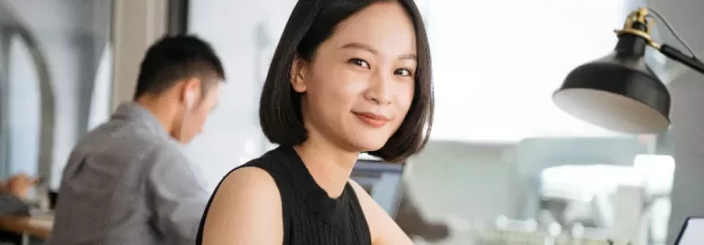 An Asian woman in a sleeveless top smiling to the camera in an office setting