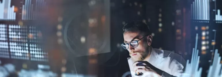 Man analyzing data on a computer screen with graphs in a dimly lit room.