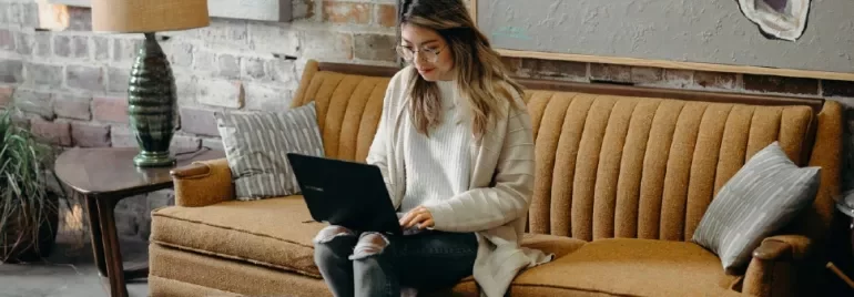 Person sitting on a brown couch using a laptop.