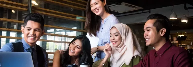 Diverse group of five people smiling around a laptop in an office setting.