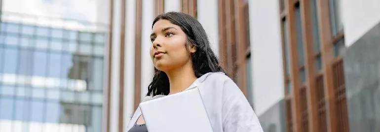 Person holding a laptop standing outside a modern building