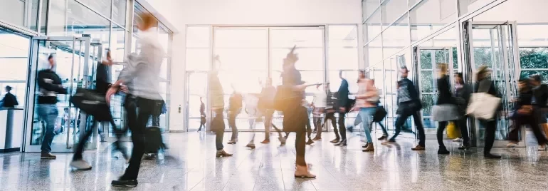 Blurred motion of people walking through a modern glass entrance.