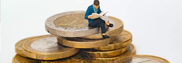 A male figurine sitting on a pile of gold coins reading a newspaper