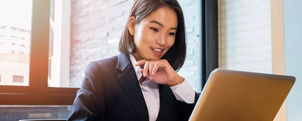 Person in a suit working on a laptop near a sunlit window.