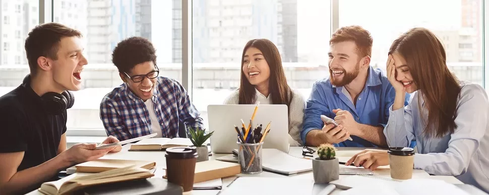 Group of diverse students laughing and studying together in a bright room.