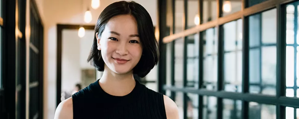 Person smiling in a modern office hallway with glass walls.
