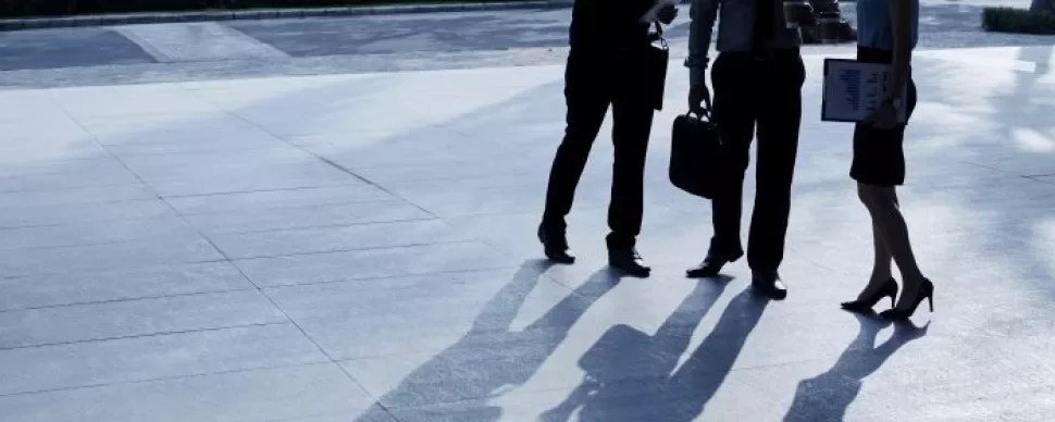 Three business professionals standing together in front of a modern office building, engaged in conversation.