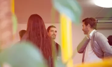 Three people having a conversation in an office setting with plants in the foreground.