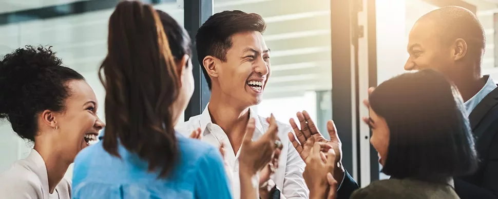 Group of diverse coworkers smiling and clapping in an office setting.