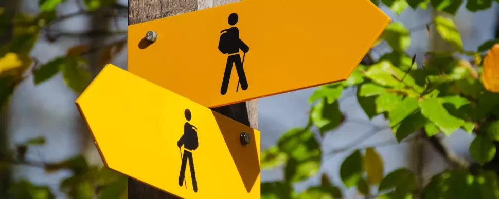 Two yellow hiking trail signs with black hiker icons on a wooden post