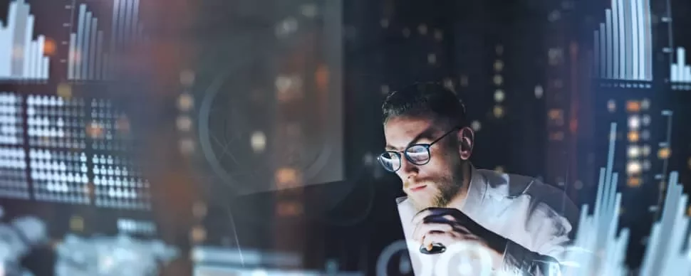 Man analyzing data on a computer screen with graphs in a dimly lit room.