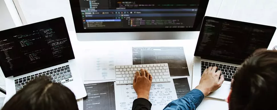 Three people working on laptops with code on the screens.
