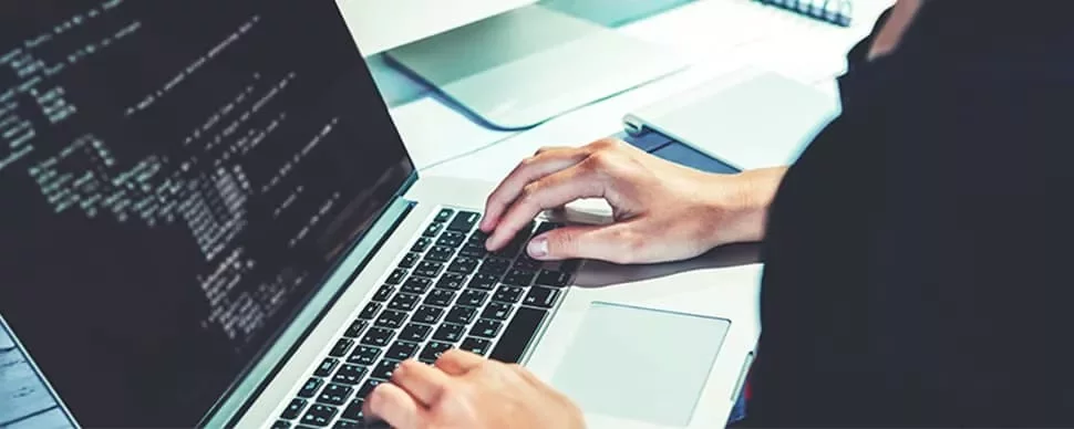 Person typing on a laptop with code on the screen.