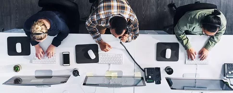 Overhead view of three people working at computers in an office.