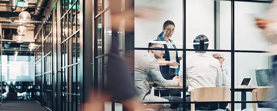 Business meeting in a modern glass-walled office with people discussing.