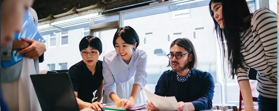 A diverse team collaborating around a laptop in a bright office setting.