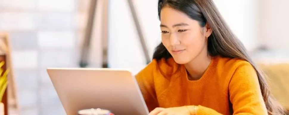 Woman in orange sweater using a laptop at a desk.