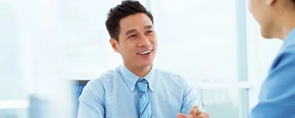 Man in blue shirt smiling during a meeting in a bright office.
