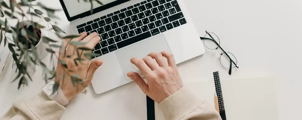 Person typing on a laptop with notebook and glasses on a desk.