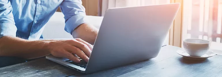 Person typing on a laptop at a wooden desk with a cup of coffee.